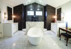 A white, tiled bathroom. The bathtub sits prominently in the center of the room. very well lit, with white marble and black tile in the background