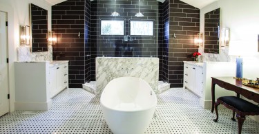 A white, tiled bathroom. The bathtub sits prominently in the center of the room. very well lit, with white marble and black tile in the background